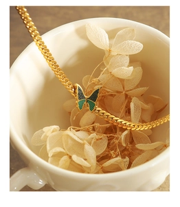 Makro-Detail einer goldenen Schmetterlingskette mit Emaille-Flügeln in dekorativer Tasse