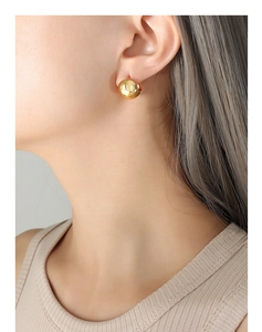 Detailed view of polished gold spherical stud earrings worn by a model in soft light
