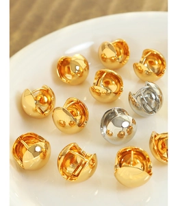Macro view of polished gold and silver spherical stud earrings on a ceramic dish