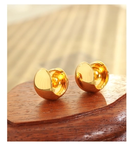 Detailed view of polished thick golden C-shaped hoop earrings on a red wooden stand