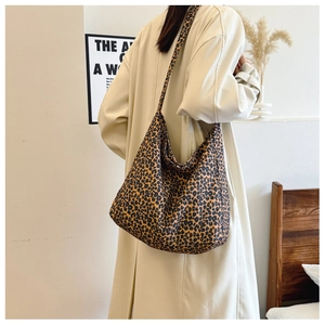 Leopard print canvas tote bag shown worn over the shoulder by a model in soft warm lighting