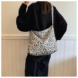 Detailed back view of a large leopard print canvas crossbody bag worn by a model