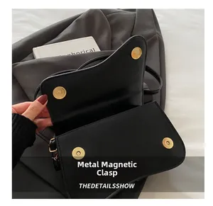 Close-up of elegant asymmetric flap with luxury gold magnetic buckle on black leather bag