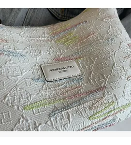 Detailed macro view of quilted canvas bag featuring colorful wavy embroidery and brand label