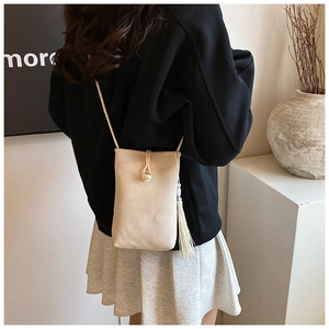 Detail of a beige mini crossbody phone bag with pearl closure and tassel on a model