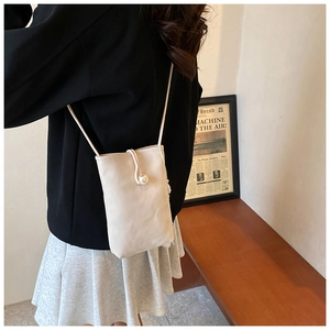 Vertical cream crossbody phone bag with large pearl clasp detail on a model's side