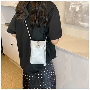 Silver cross-body phone bag with pearl buckle and tassel detail on a female model