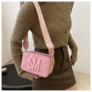 Sac bandoulière rose avec logo SM 3D et large bandoulière tissée géométrique porté par mannequin