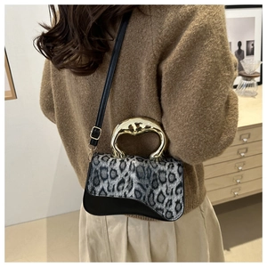 Detail of leopard print crossbody bag with gold sculptural handle in home setting
