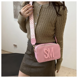 Gros plan du sac bandoulière en cuir rose avec logo SM et bandoulière tissée large