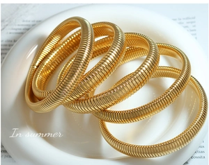 Close-up of four stacked gold-plated bracelets with fine ribbed texture on a white plate