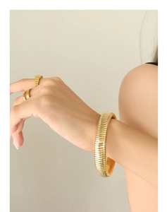 Close-up of gold minimalist textured cuff bracelet and smooth rings on model's wrist