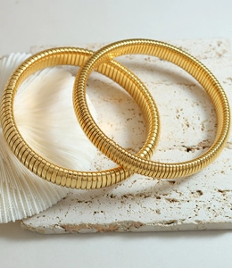 Macro detail of 18k gold plated gaspipe style flexible bracelets on stone surface