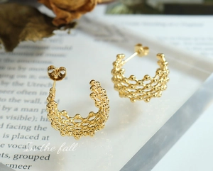 Macro view of 18K gold-plated C-shaped dreamcatcher earrings with woven bead texture