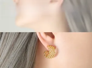 Detail shot of golden C-shaped dreamcatcher earrings featuring intricate hollow mesh patterns
