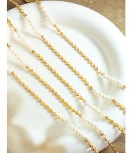 Détail du collier de perles d'eau douce et perles carrées dorées sur une assiette blanche