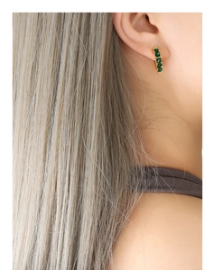 Détail de boucles d'oreilles C en or 18K avec zircons verts sur un mannequin femme