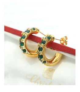 Détail macro de boucles d'oreilles dorées en C avec zircons émeraudes sur fond rouge