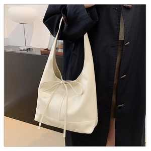Detail of a creamy white pleated tote bag with a minimalist slim leather bow accent