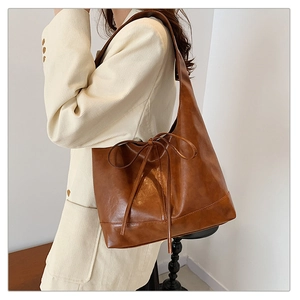 Caramel leather tote bag featuring a pleated design and decorative bow on shoulder strap
