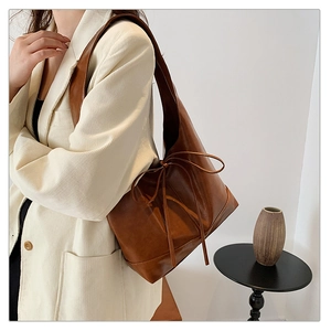 Detail of dark brown leather tote bag with elegant bow tie detail on cream corduroy blazer