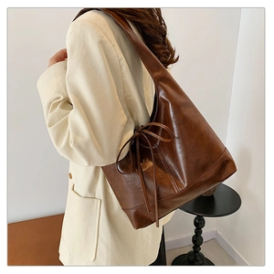Detail of a brown PU leather tote bag featuring a bow drawstring and minimalist design