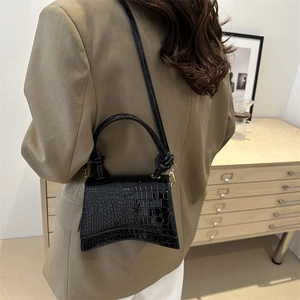 Chic black crocodile embossed leather handbag with curved base on model in brown blazer