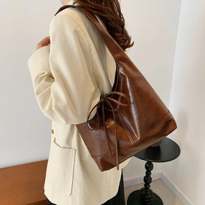 Brown leather pleated tote bag with bow detail shown on a model in a minimalist room