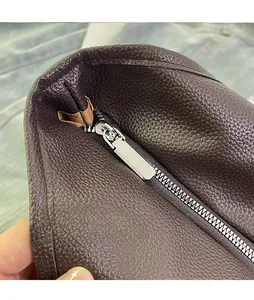 Detail showing the front zipper design and rich lychee grain leather of the dark brown bag