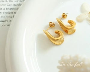 Close-up of matte gold irregular curved earrings with brushed texture on vintage background