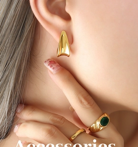 Detail of model wearing gold arched earrings and retro emerald gemstone ring