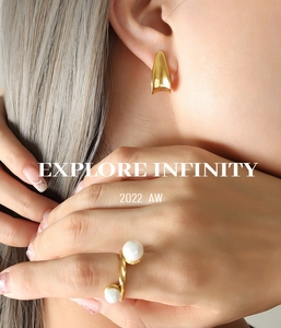 Detail of matte gold J-shaped earrings and spiral pearl ring on model in 2022 AW collection