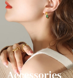 Détail des boucles d'oreilles émeraude vintage et des bagues dorées portées par le modèle
