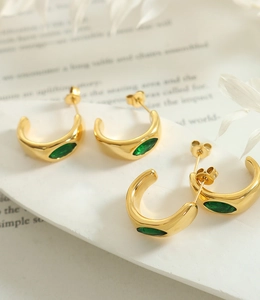 Détail de boucles d'oreilles dorées en C avec zircons émeraude sur marbre blanc
