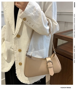 Detail of beige shoulder bag with buckle strap on a model wearing tweed jacket