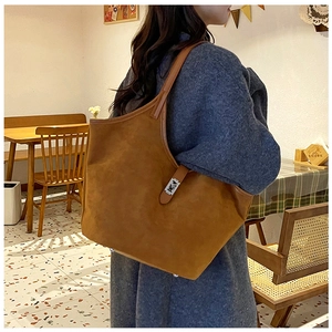 Brown suede tote bag with silver clasp shown on a model in a cozy cafe setting