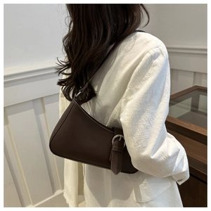 Detail of dark brown leather underarm baguette bag worn over a white textured blazer