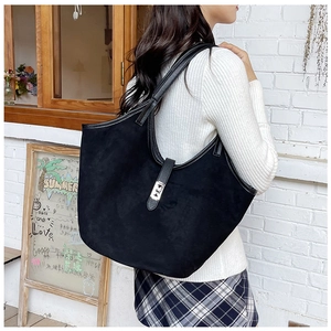 Detail of black suede tote bag featuring a silver metal turn-lock and leather shoulder strap