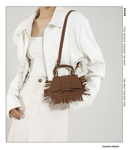 Détail d'un mini sac bandoulière marron à franges avec accessoires dorés sur une tenue blanche