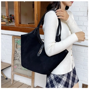 Detail of a large black suede tote bag with leather straps on a model in an outdoor cafe
