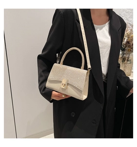 Detail of cream crossbody bag featuring shimmering rhinestone flap and gold twist lock clasp