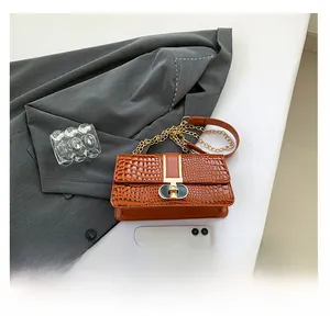 Detail of brown crocodile pattern shoulder bag with golden chain and metal clasp closure