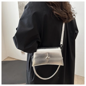 Gros plan d'un sac bandoulière argenté brillant avec boucle étoile sur manteau noir