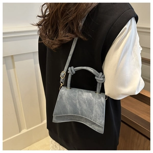 Detail of light blue denim texture bag with unique wave base and rope handle worn by model