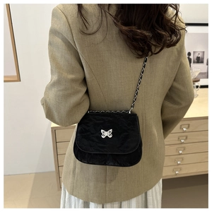 Vue détaillée d'un sac noir plissé avec boucle papillon argentée porté par un mannequin