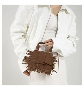 Détail du sac à main marron à franges avec boucle métallique sur une veste blanche