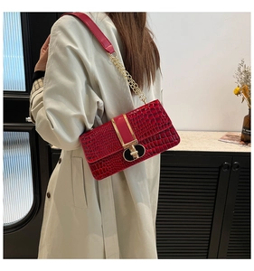 Deep red crocodile pattern shoulder bag with gold chain strap on an beige trench coat