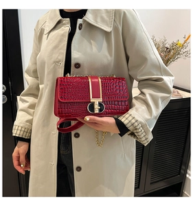 Detail of red crocodile texture handbag with gold metal lock and chain strap on model