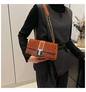 Detail of a brown crocodile pattern shoulder bag with gold chain and clasp closure