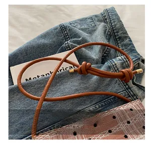 Détail d'une bandoulière en cuir marron nouée et d'un sac en dentelle à pois blanc